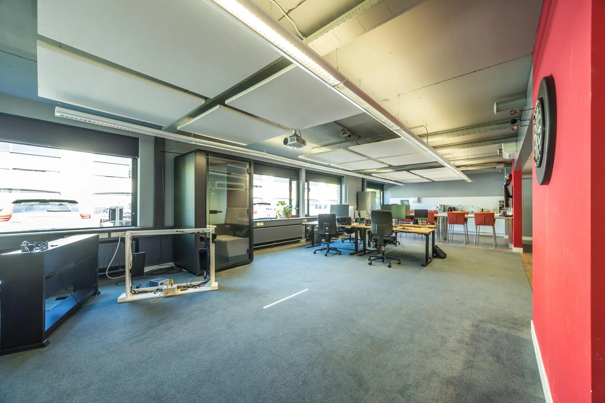 Moderne, open kantoorruimte aan de Burgemeester Verderlaan met bureaus, werkplekken, een belcel en een dartbord aan de rode muur.