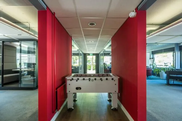 Tafelvoetbaltafel in een moderne kantoorruimte met rode muren en glazen vergaderruimtes.