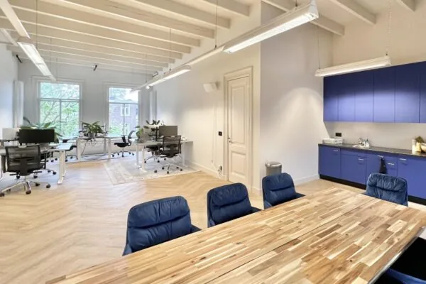 Modern kantoorinterieur aan de Paulus Potterstraat met werkplekken, vergadertafel en blauwe keukenkasten.