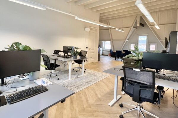 Modern kantoorinterieur aan de Paulus Potterstraat met bureaus, computerschermen en planten in een lichte ruimte met houten vloer en schuin plafond.