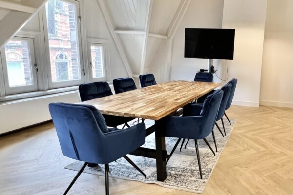 Vergaderruimte met houten tafel, acht blauwe stoelen en flatscreen-tv aan de Paulus Potterstraat.
