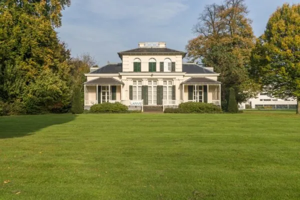 Wit landhuis Sparrenheuvel met symmetrische gevel en groene luiken, omgeven door een uitgestrekt gazon en bomen.