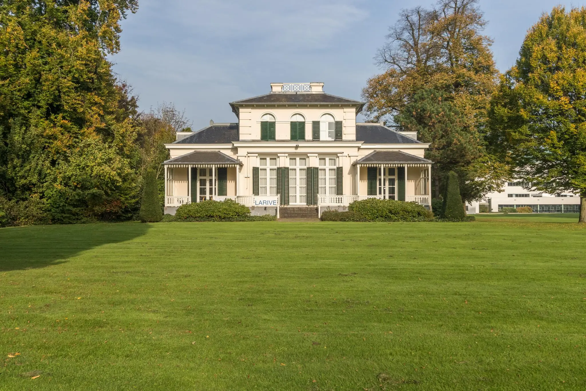 Wit landhuis Sparrenheuvel met symmetrische gevel en groene luiken, omgeven door een uitgestrekt gazon en bomen.