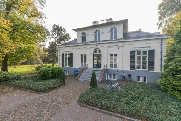 Vooraanzicht van landhuis Sparrenheuvel met trap, symmetrische ramen en omliggende tuin.