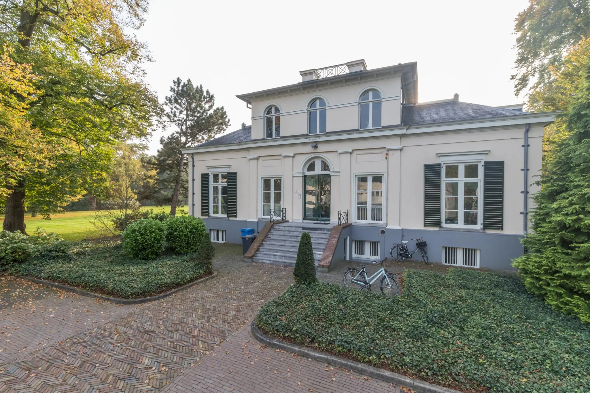 Vooraanzicht van landhuis Sparrenheuvel met trap, symmetrische ramen en omliggende tuin.