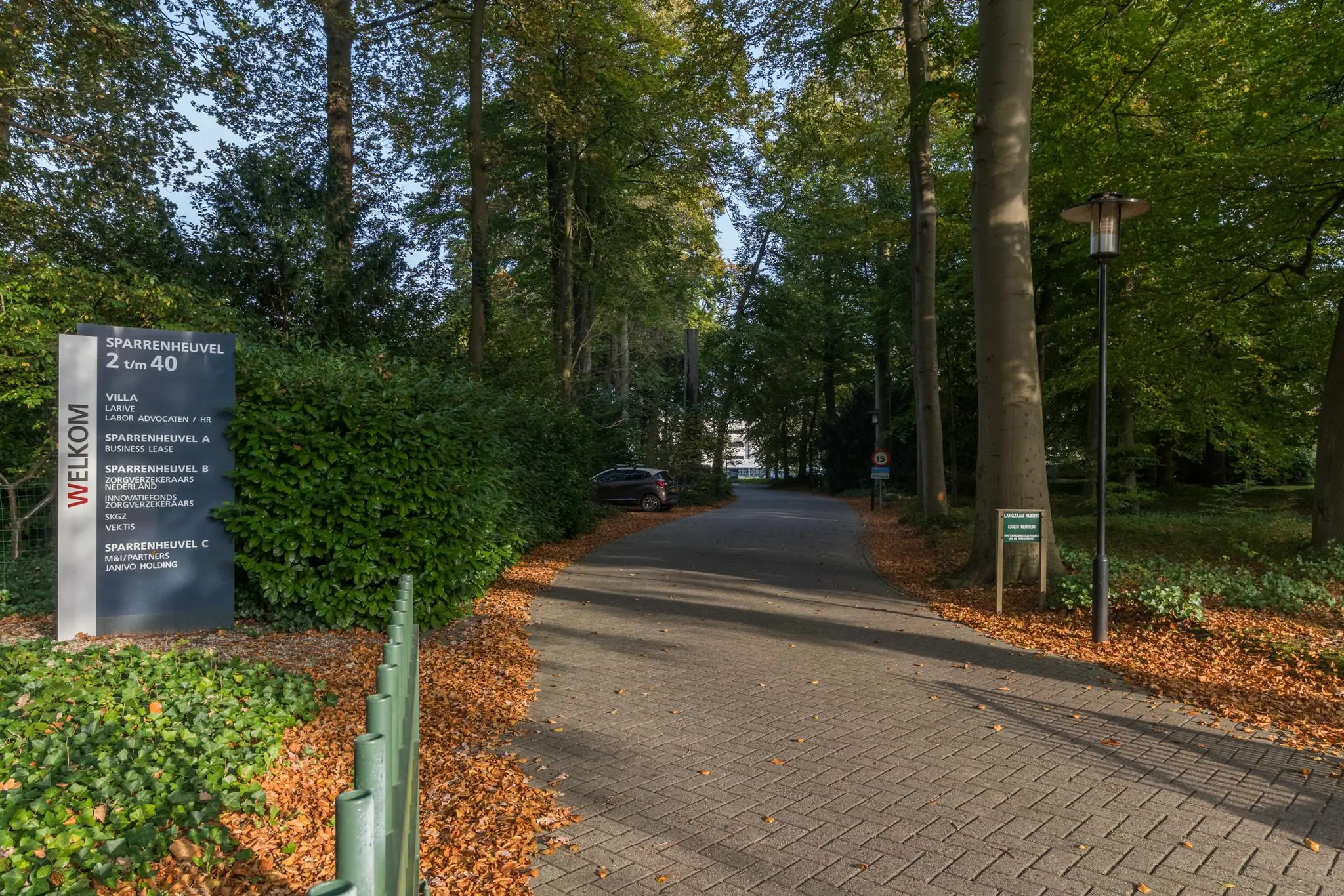Oprit naar bedrijventerrein Sparrenheuvel met omringende bomen en een informatiebord bij de ingang.