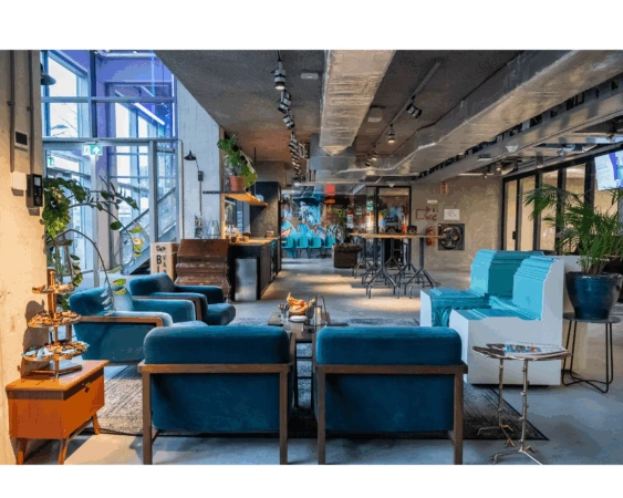 Moderne, kleurrijke lounge- en werkruimte aan de Wibautstraat met blauwe meubels, planten en een creatieve, industriële inrichting.