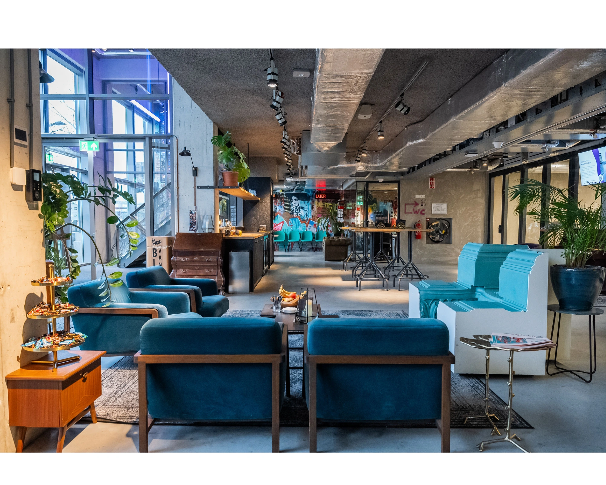 Moderne, kleurrijke lounge- en werkruimte aan de Wibautstraat met blauwe meubels, planten en een creatieve, industriële inrichting.