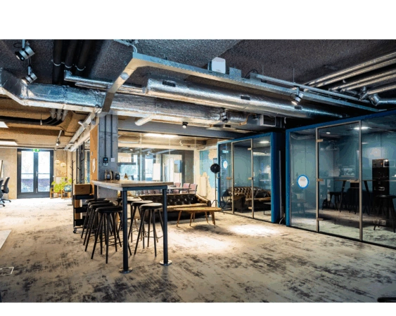 Modern ingerichte kantoorruimte aan de Wibautstraat met glazen vergaderruimtes, industriële details en een gemeenschappelijke zithoek.