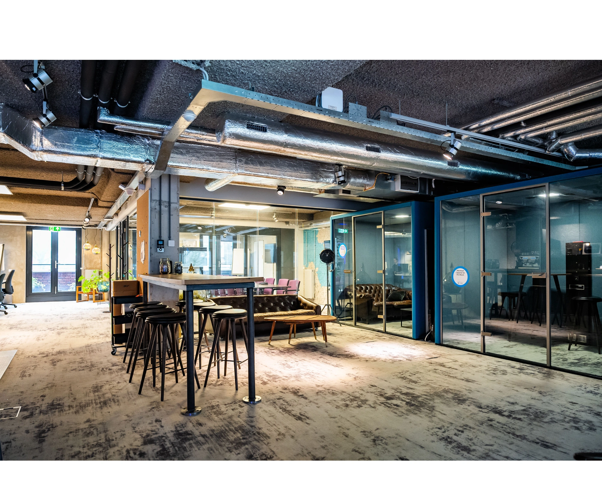 Modern ingerichte kantoorruimte aan de Wibautstraat met glazen vergaderruimtes, industriële details en een gemeenschappelijke zithoek.