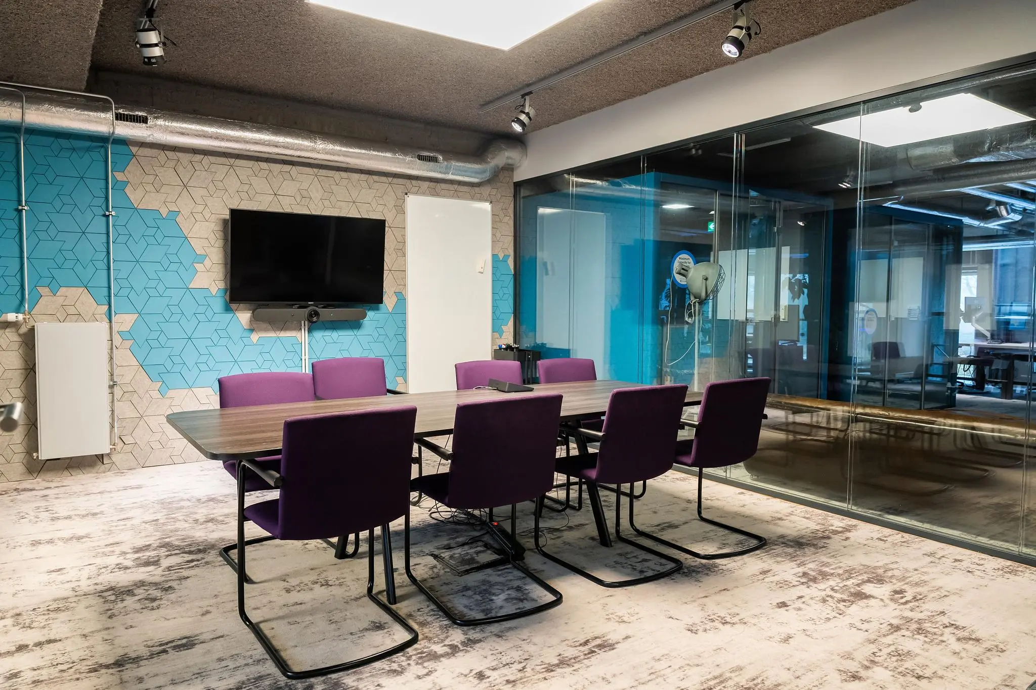 Vergaderruimte aan de Wibautstraat met een lange tafel, paarse stoelen, een flatscreen en glazen wanden.