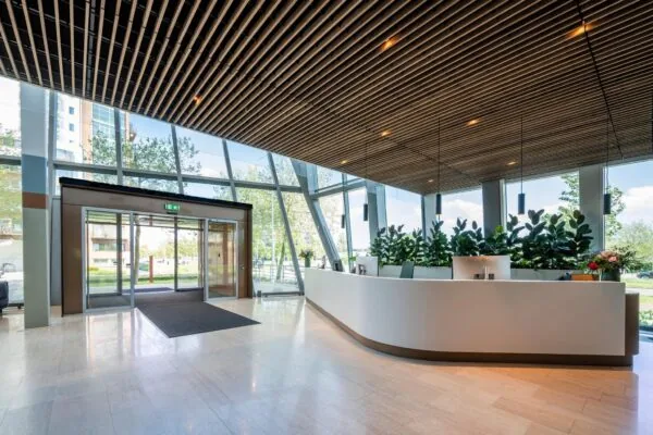 Moderne en lichte ontvangstruimte aan de David Ricardostraat met een gebogen balie, grote glazen gevel en houten plafond.