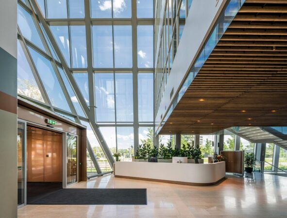 Moderne, lichte entreehal van een kantoorgebouw aan de David Ricardostraat met glazen gevel, houten plafond en een receptiebalie.