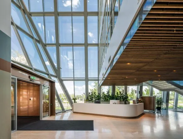 Moderne, lichte entreehal van een kantoorgebouw aan de David Ricardostraat met glazen gevel, houten plafond en een receptiebalie.