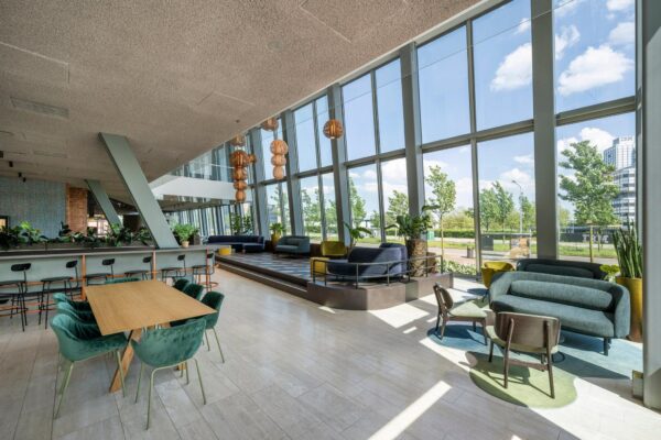 Moderne, licht ingerichte lounge met grote ramen aan de David Ricardostraat met uitzicht op groen en een IBM-kantoorgebouw.