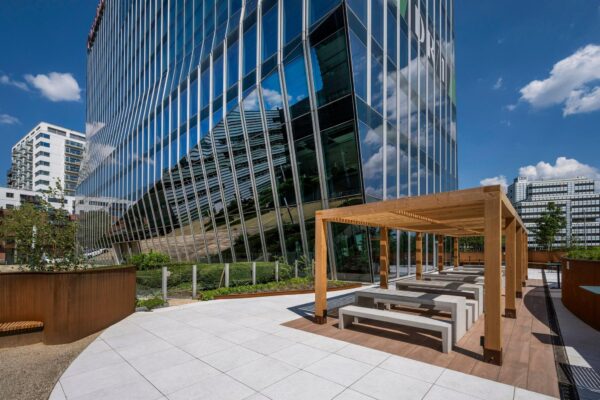 Moderne kantoorgebouwen aan de David Ricardostraat met een houten pergola en picknickbanken op een zonnig terras.