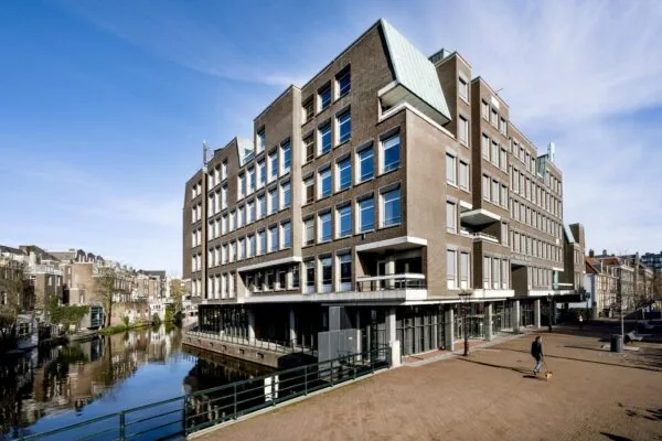 Modern kantoorgebouw aan de Vijzelgracht in Amsterdam met uitzicht op de gracht en een wandelaar met hond op de voorgrond.