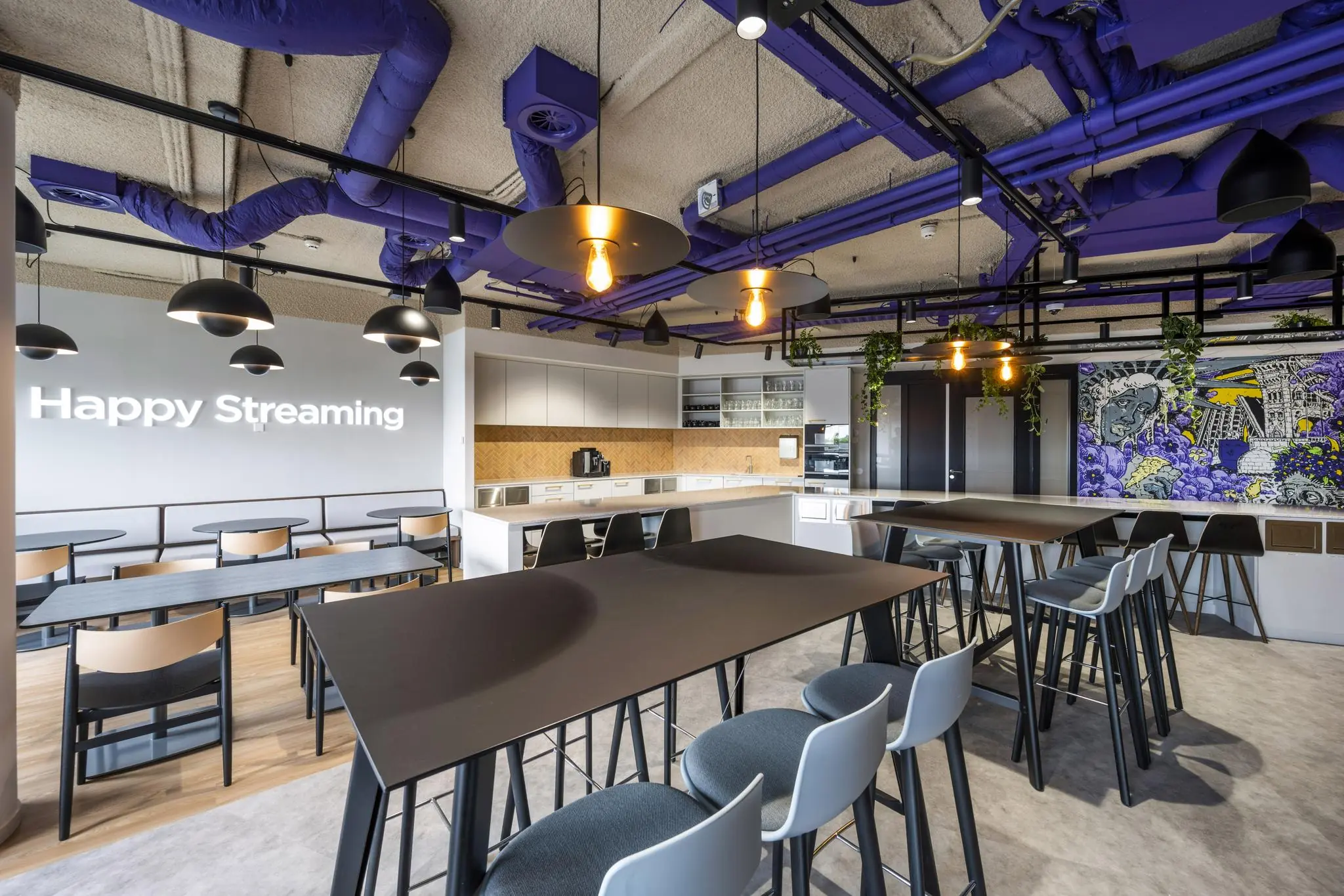 Moderne bedrijfskeuken en lunchruimte aan de Vijzelgracht met paarse leidingen, industriële verlichting en muurschildering.