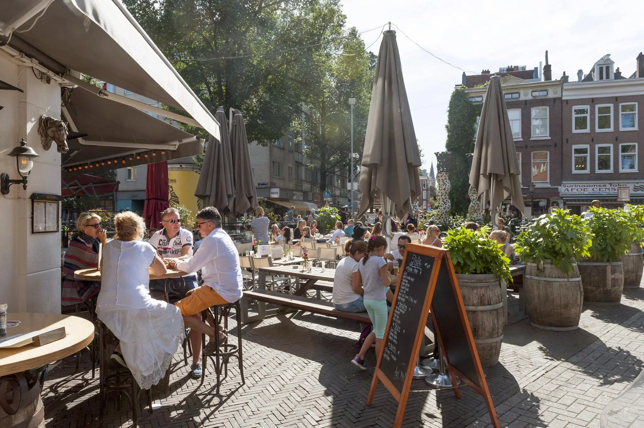 Drukke terrasscene op de Vijzelgracht in Amsterdam met mensen die ontspannen in de zon zitten.