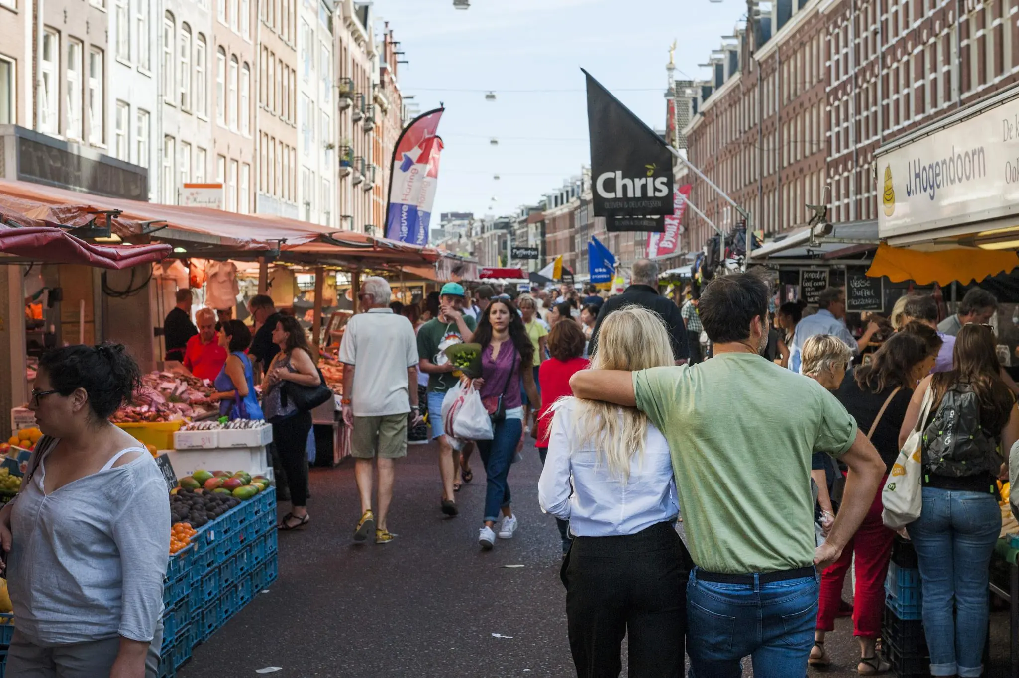 Drukke marktdag op de Vijzelgracht in Amsterdam met mensen die langs kramen met groenten, fruit en andere producten lopen.