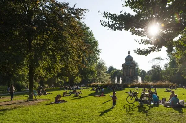 Mensen ontspannen op het gras in het zonnige Vondelpark bij de Vondelmonument fontein in Amsterdam.