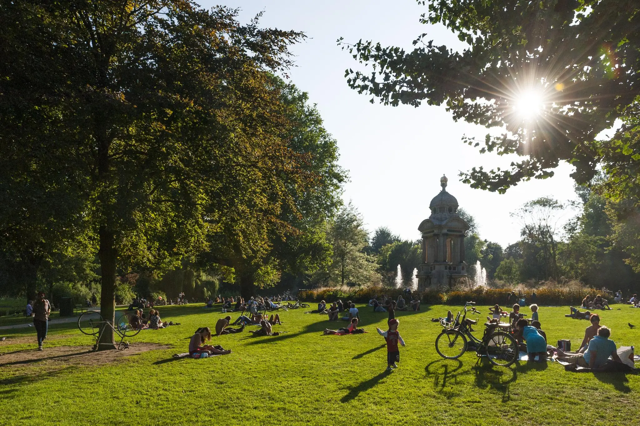 Mensen ontspannen op het gras in het zonnige Vondelpark bij de Vondelmonument fontein in Amsterdam.