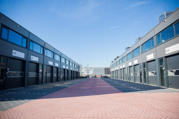 Moderne bedrijfsunits aan de Laan van ’s-Gravenmade met industriële gevels en roldeuren onder een heldere blauwe lucht.