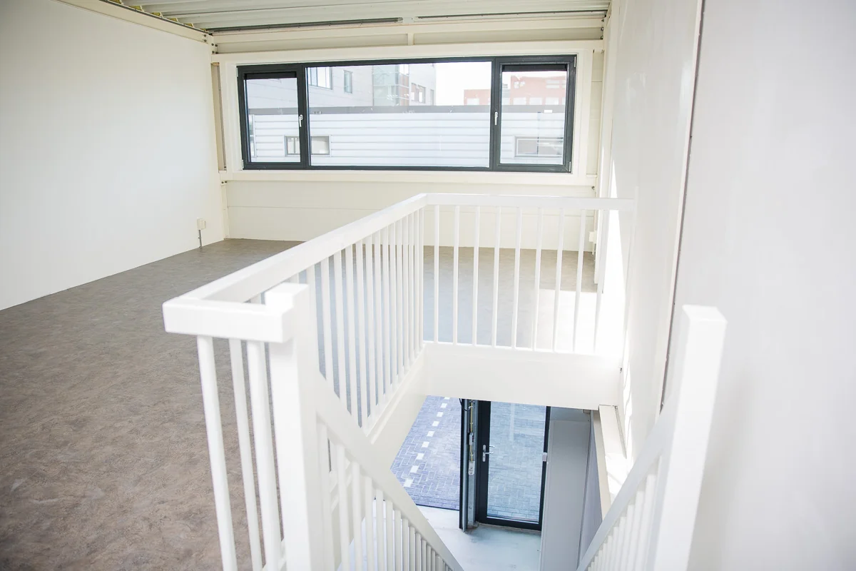 Licht en modern trappenhuis in bedrijfsruimte aan de Laan van s-Gravenmade met grote ramen en strak interieur.