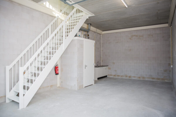 Lege bedrijfsruimte aan de Laan van 's-Gravenmade met betonnen vloer, witte trap, keukentje en techniekruimte.
