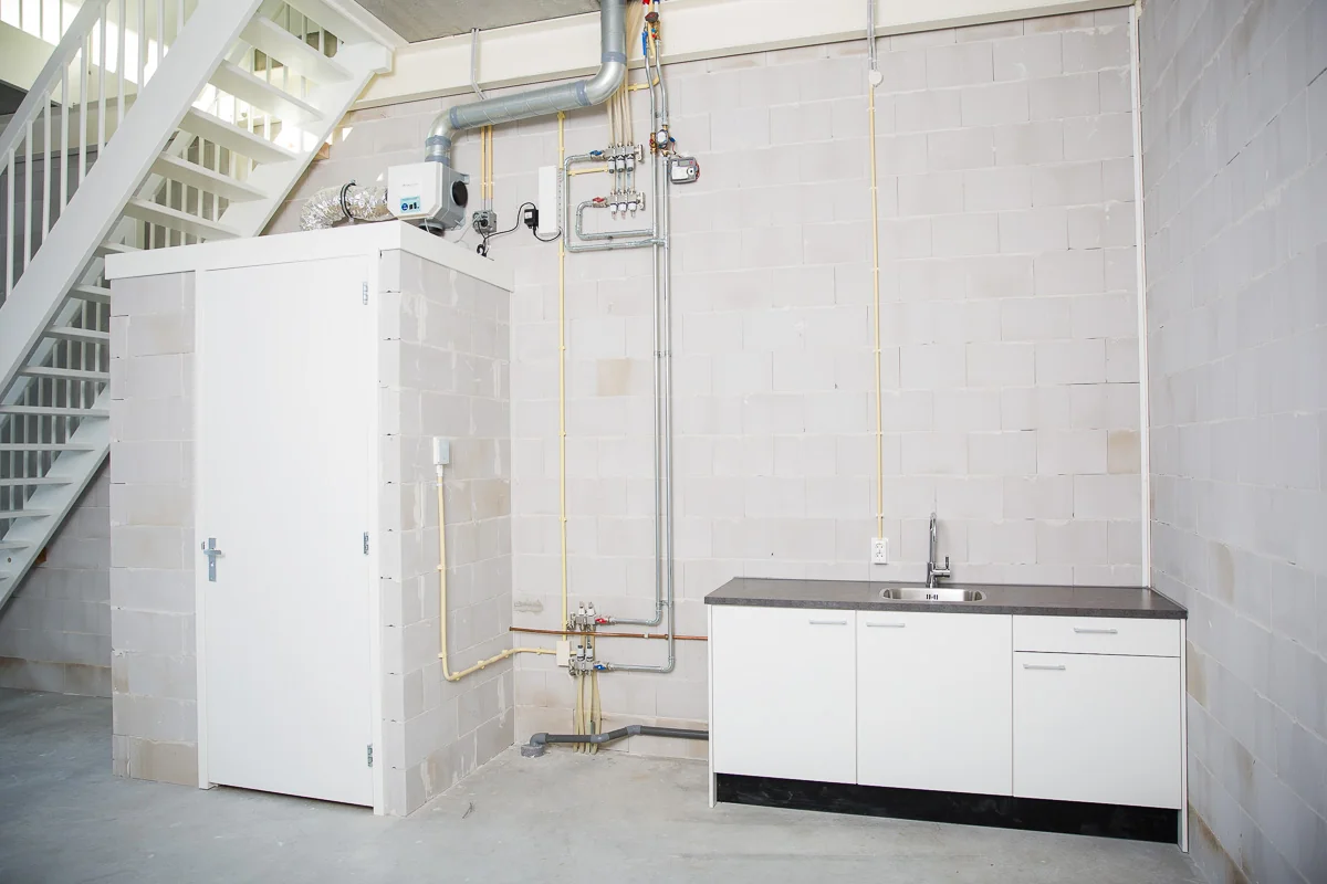 Kleine pantry met wit keukenblok en technische installaties in een bedrijfsruimte aan de Laan van 's-Gravenmade.
