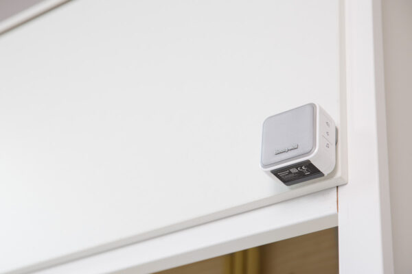 Een witte Honeywell deurbel is gemonteerd op een deurkozijn in een modern interieur aan de Laan van ’s-Gravenmade.