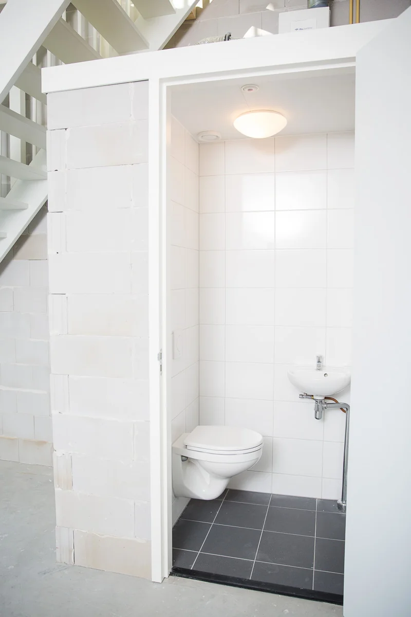Kleine, witte toiletruimte met hangtoilet en fonteintje onder een trap in een casco bedrijfsruimte aan de Laan van s-Gravenmade.