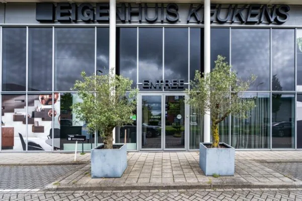 Vooraanzicht van de entree van Eigenhuis Keukens aan de Cornusbaan, met twee olijfbomen in plantenbakken.