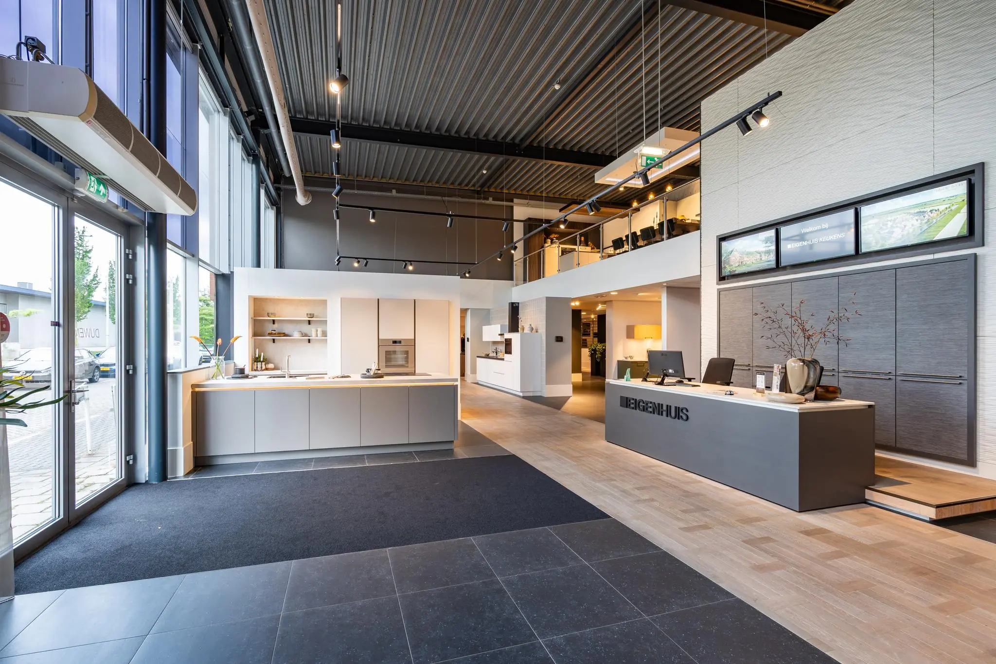 Moderne showroom van Eigenhuis met een stijlvolle receptiebalie, open keukenopstelling en vergaderruimte op de bovenverdieping.