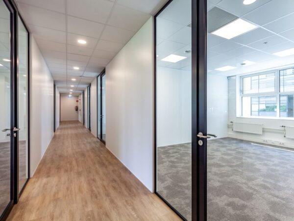 Een moderne kantoorhal met glazen deuren en zicht op een lege kantoorruimte.