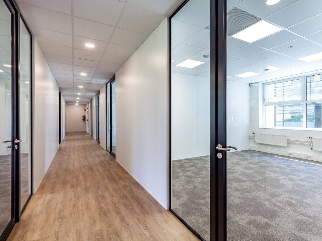Een moderne kantoorhal met glazen deuren en zicht op een lege kantoorruimte.