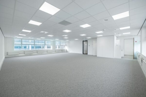 Een ruime, lege kantoorruimte met grijs tapijt en grote ramen.