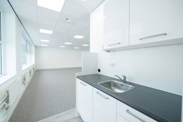 Een lege, moderne kantoorruimte met een kleine keukenhoek en veel natuurlijk licht.