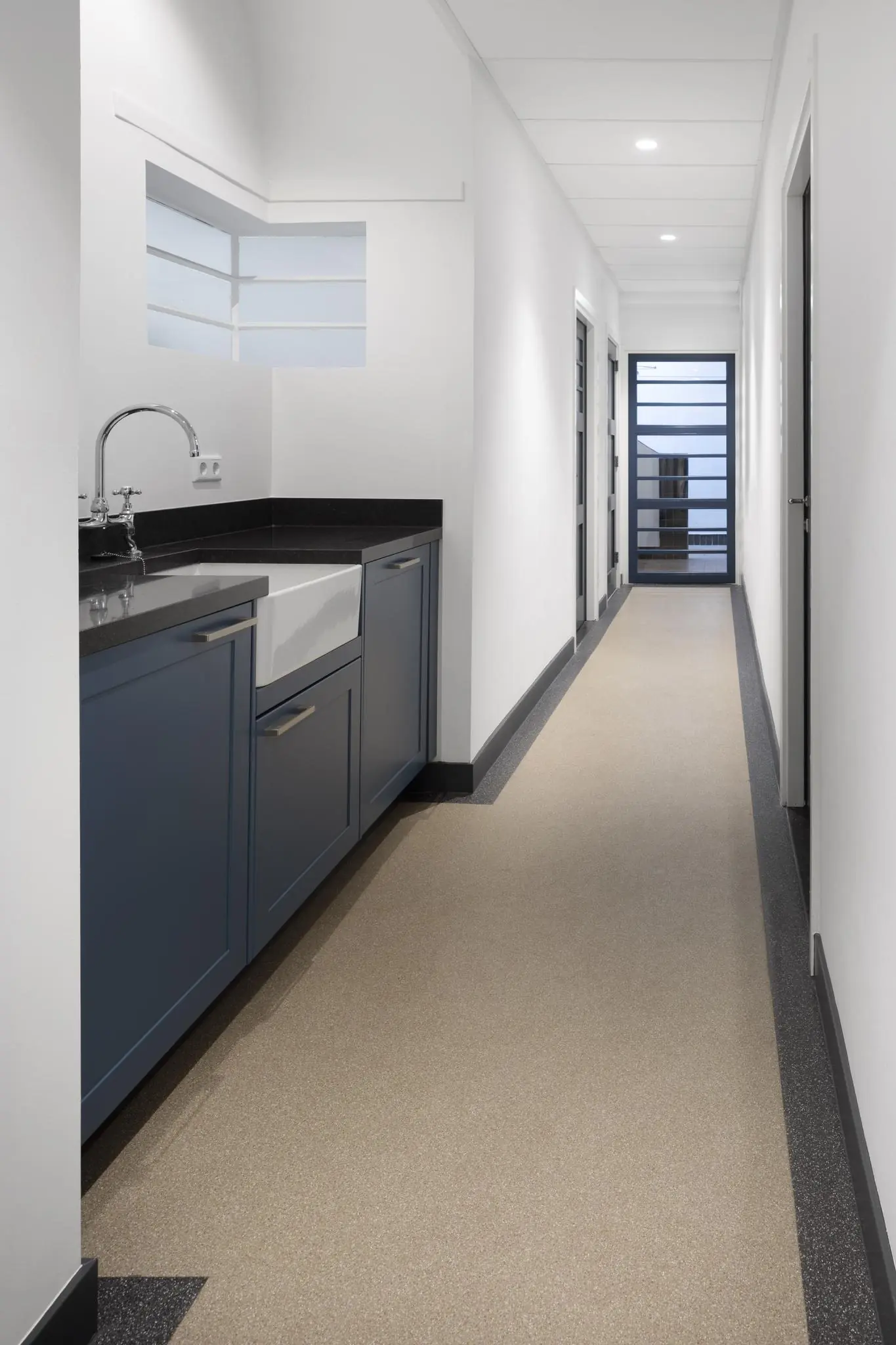 Lange, smalle gang in een woning aan de Hillegomstraat met een keukenblok met blauwe kastjes en zwarte aanrechtblad.