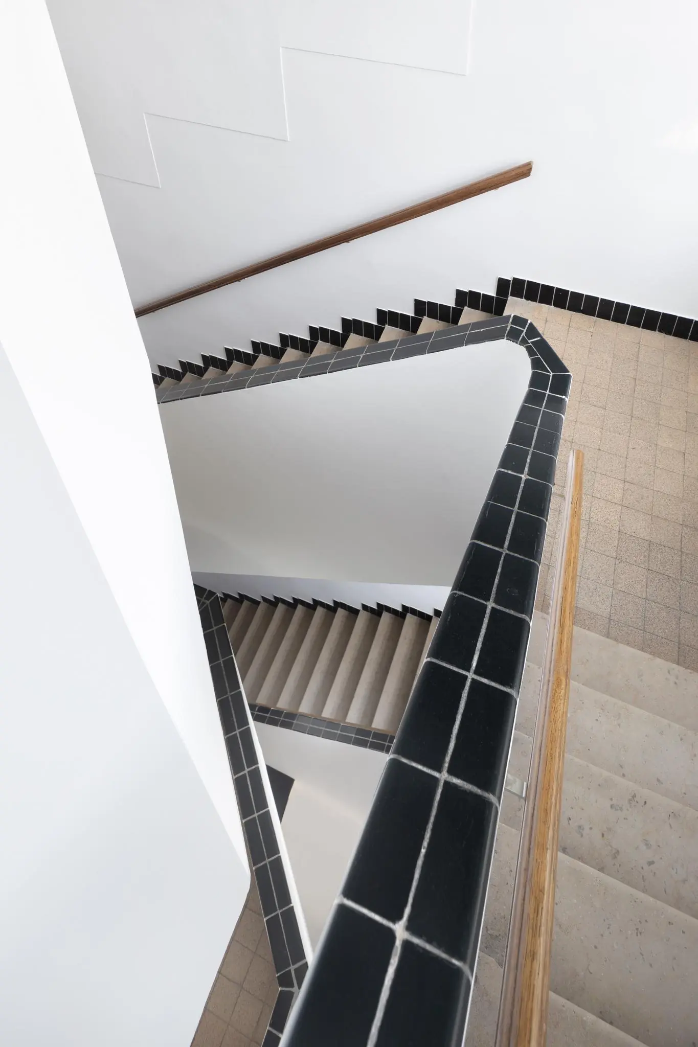 Trapportaal in de Hillegomstraat met betegelde zwarte leuningen en beige stenen traptreden in een strak wit interieur.