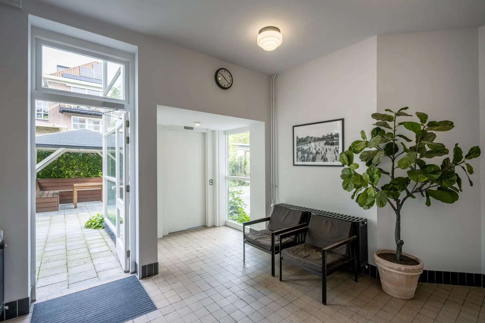 Entreehal van een appartementencomplex aan de Hillegomstraat met zitbankjes, een plant, een lift en toegang tot een binnentuin.