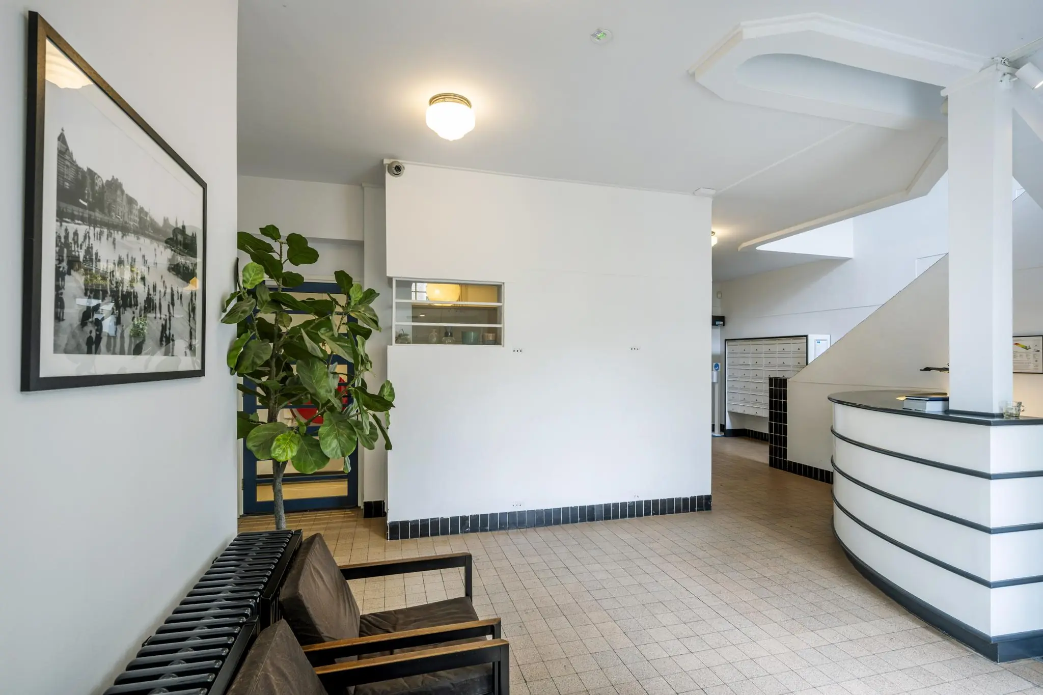 Entreehal van een appartementencomplex aan de Hillegomstraat met zitgedeelte, plant, balie en postbussen.