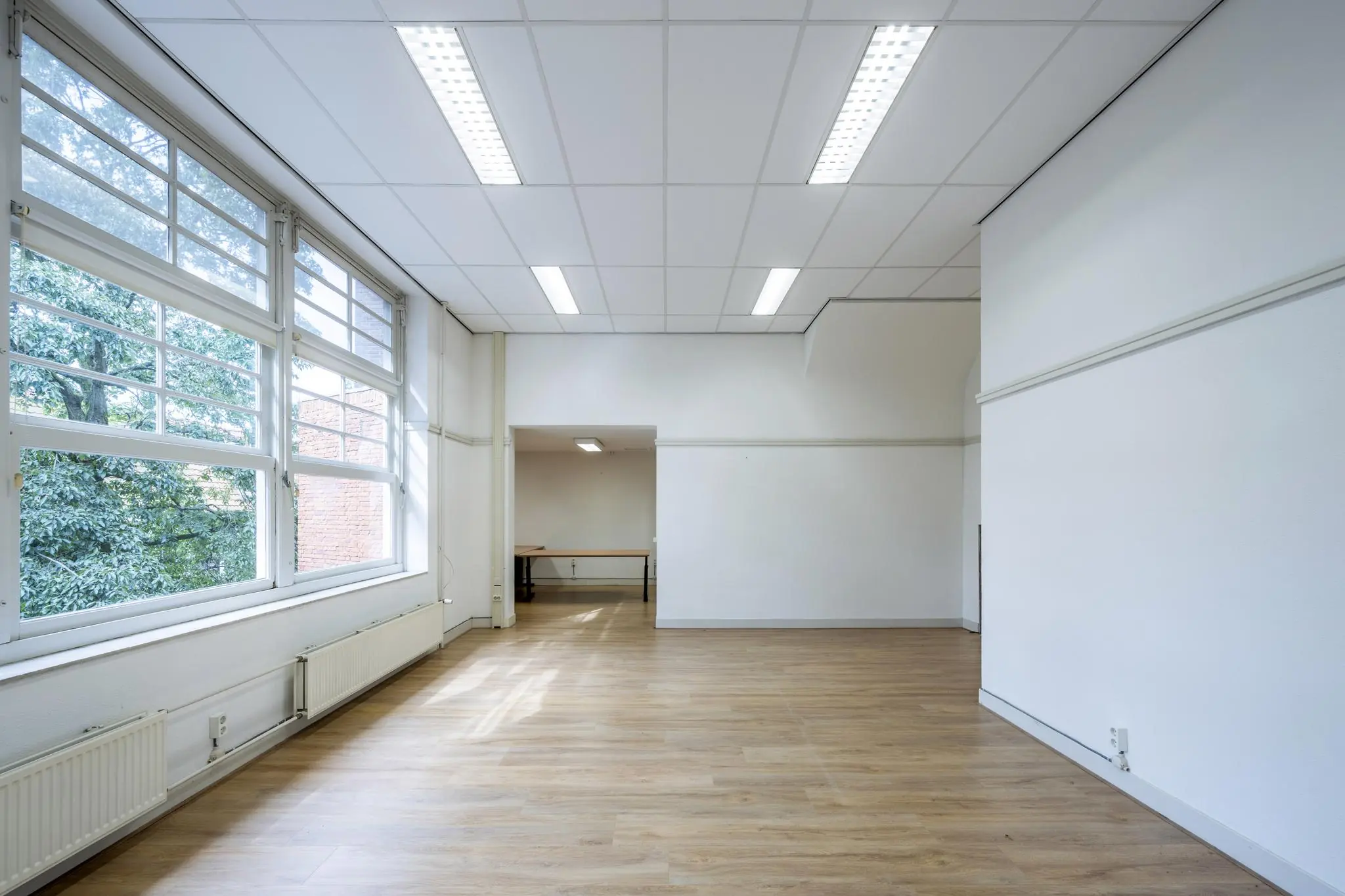 Lichte, lege ruimte aan de Hillegomstraat met grote ramen, wit plafond en houten vloer.