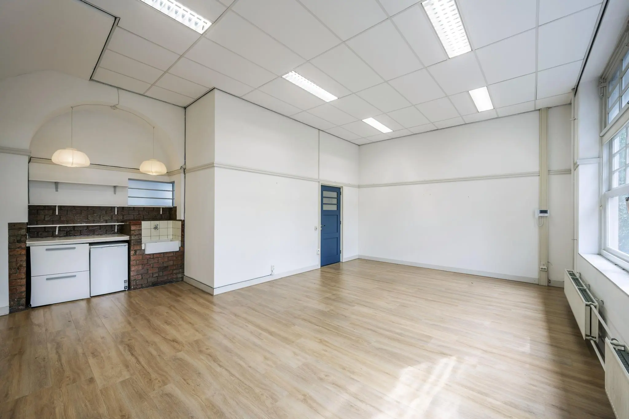 Lichte, lege ruimte aan de Hillegomstraat met houten vloer, systeemplafond, kitchenette en blauwe deur.