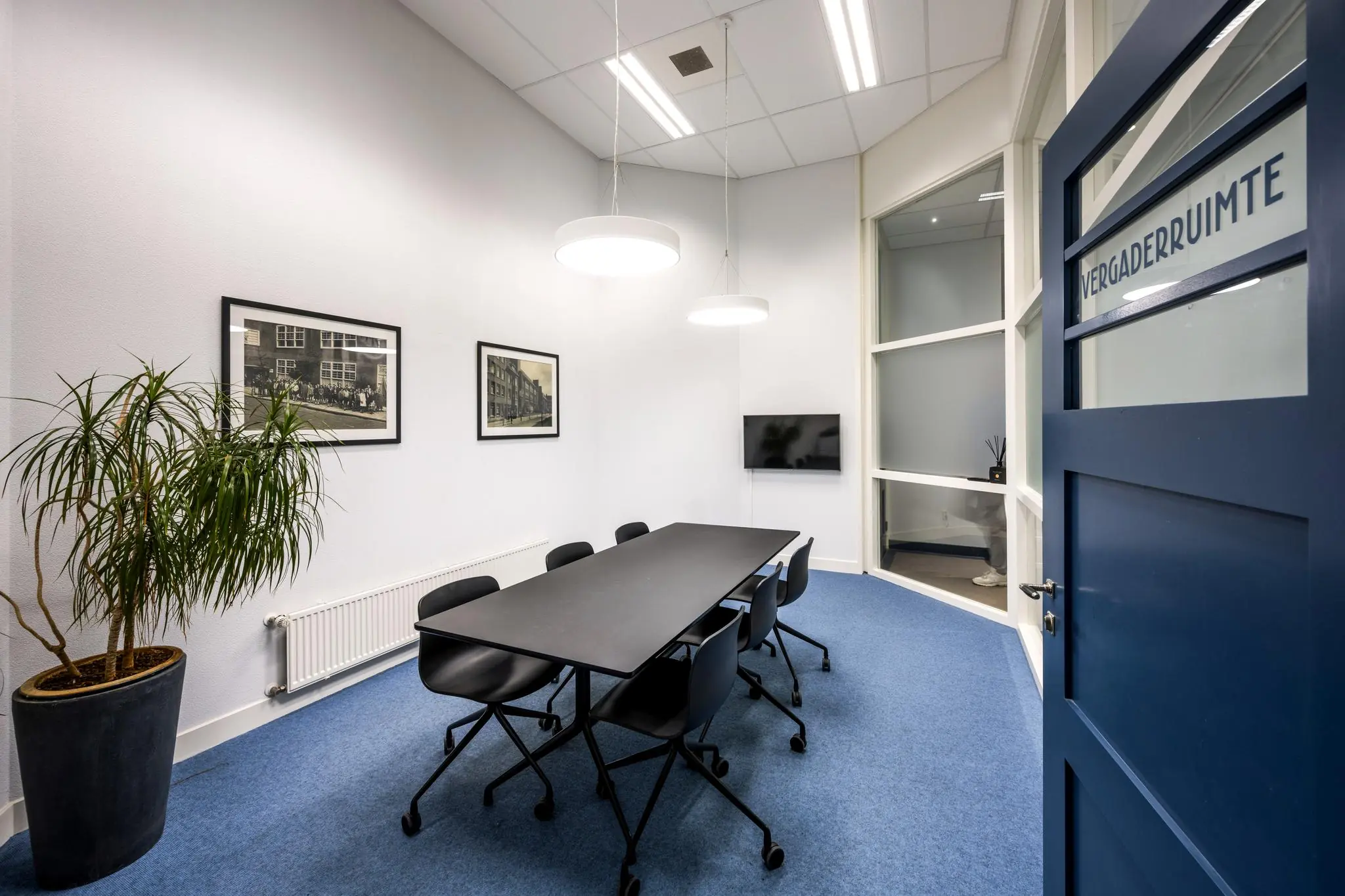 Moderne vergaderruimte aan de Hillegomstraat met een zwarte vergadertafel, zes stoelen, wanddecoratie en een flatscreen-tv.