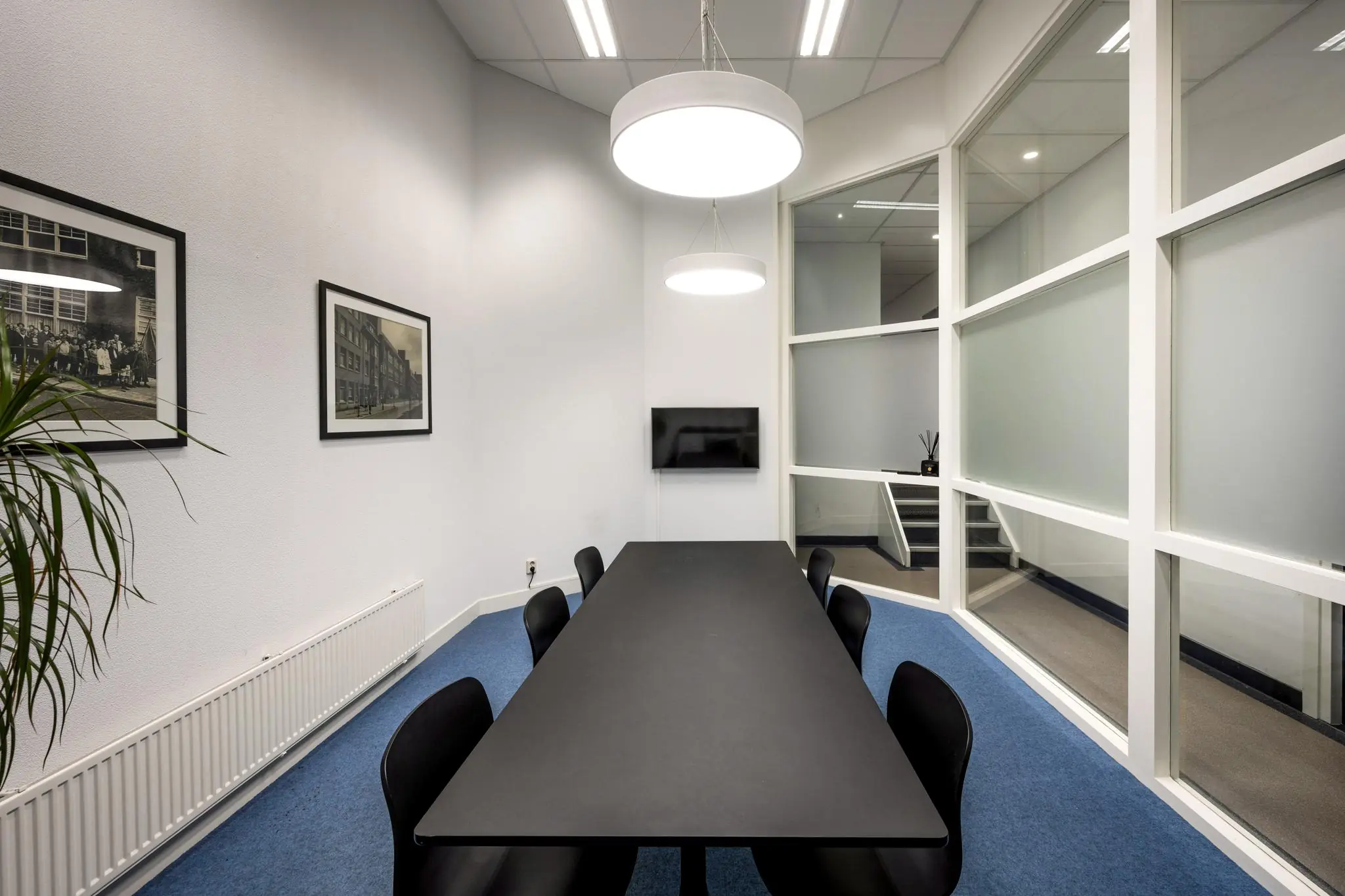Moderne vergaderruimte aan de Hillegomstraat met zwarte tafel, blauwe vloerbedekking en grote glazen wanden.