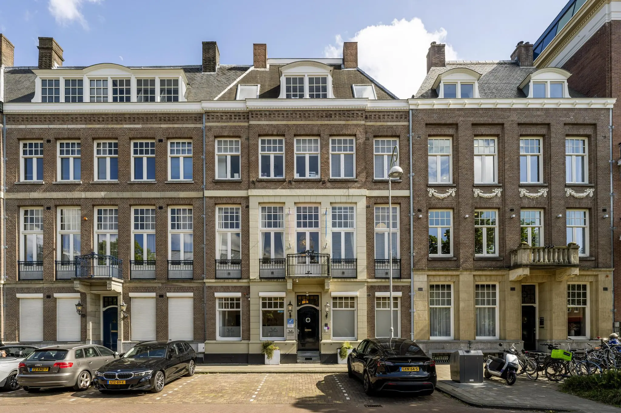 Rijtje statige herenhuizen aan het Concertgebouwplein in Amsterdam met geparkeerde auto's en fietsen op de voorgrond.