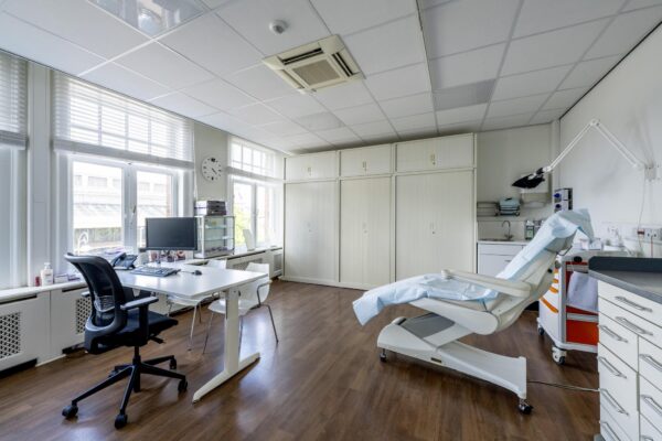 Moderne medische behandelkamer met onderzoeksstoel, bureau en computer, gelegen aan het Concertgebouwplein.