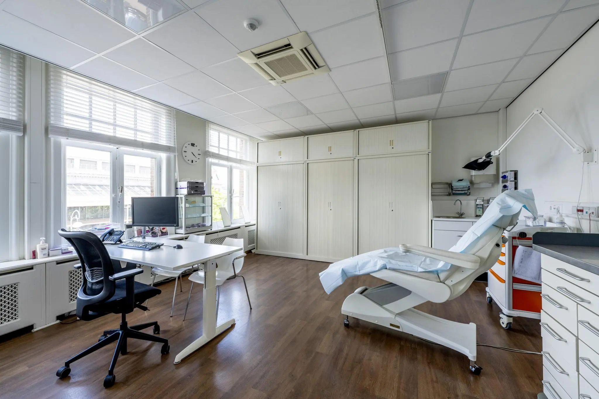 Moderne medische behandelkamer met onderzoeksstoel, bureau en computer, gelegen aan het Concertgebouwplein.