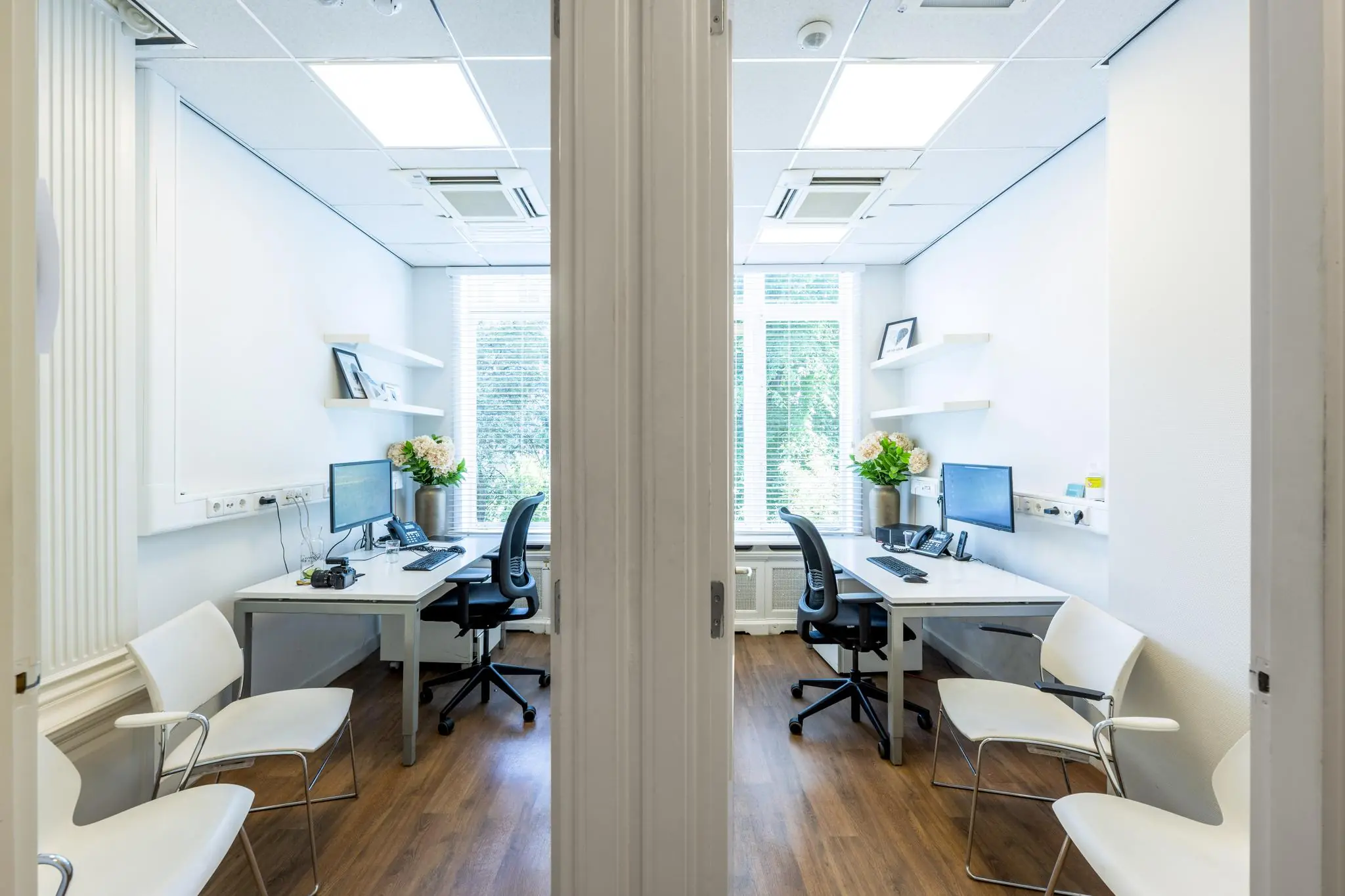 Twee modern ingerichte spreek- of werkruimtes in een licht kantoor aan het Concertgebouwplein, gescheiden door een openstaande deur.
